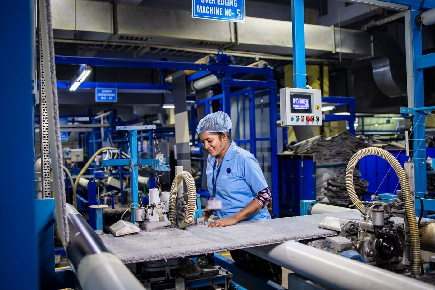 A machine operator in a hairnet and uniform working at a production machine on a factory floor