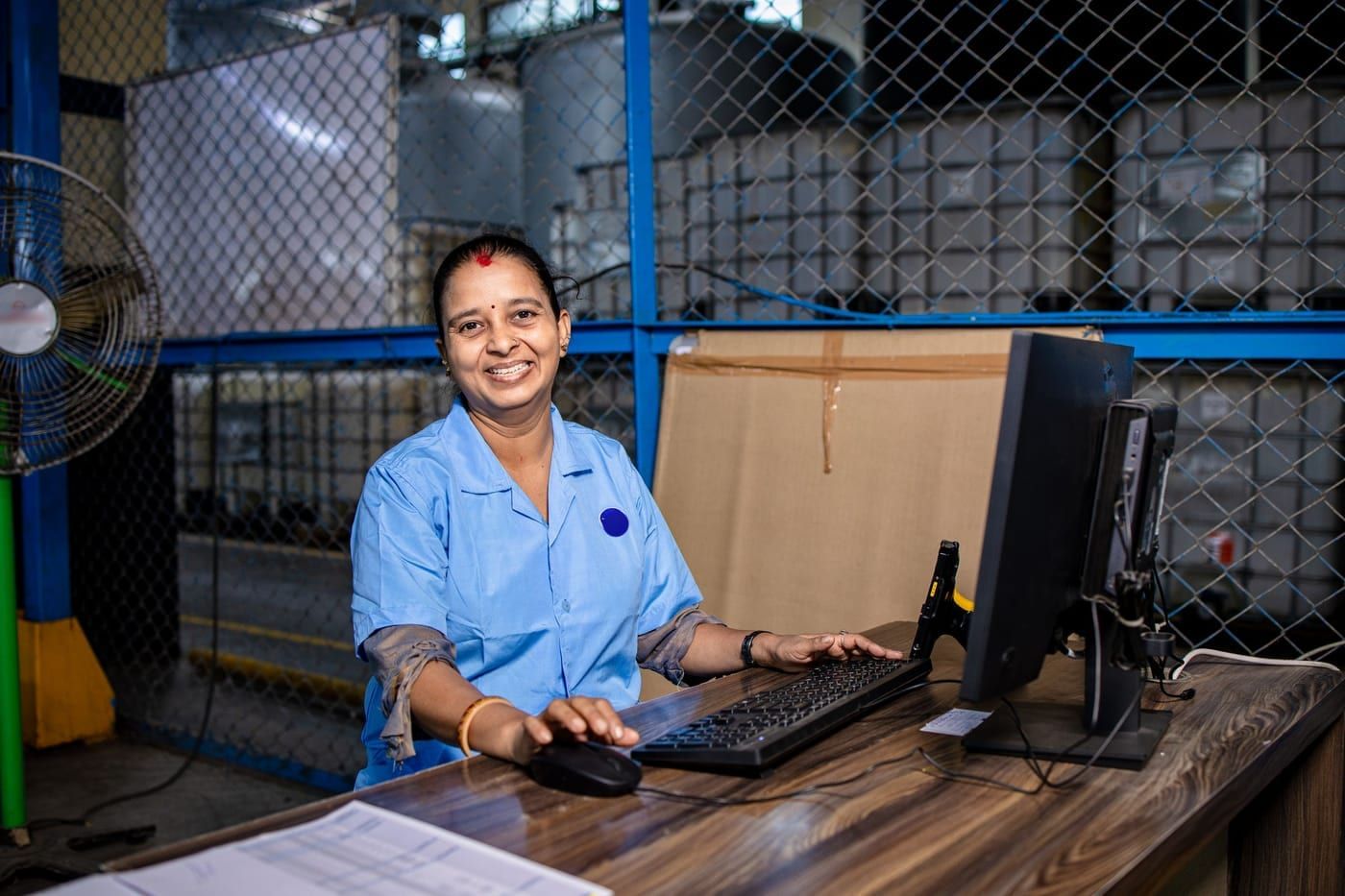 A smiling woman working at a computer in a factory office