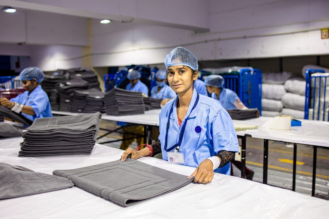 A packer stacking folded mats on a packing table on a factory floor