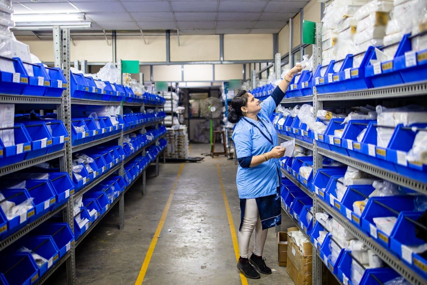 A stores worker reaching for a part on shelves of blue bins in a factory store