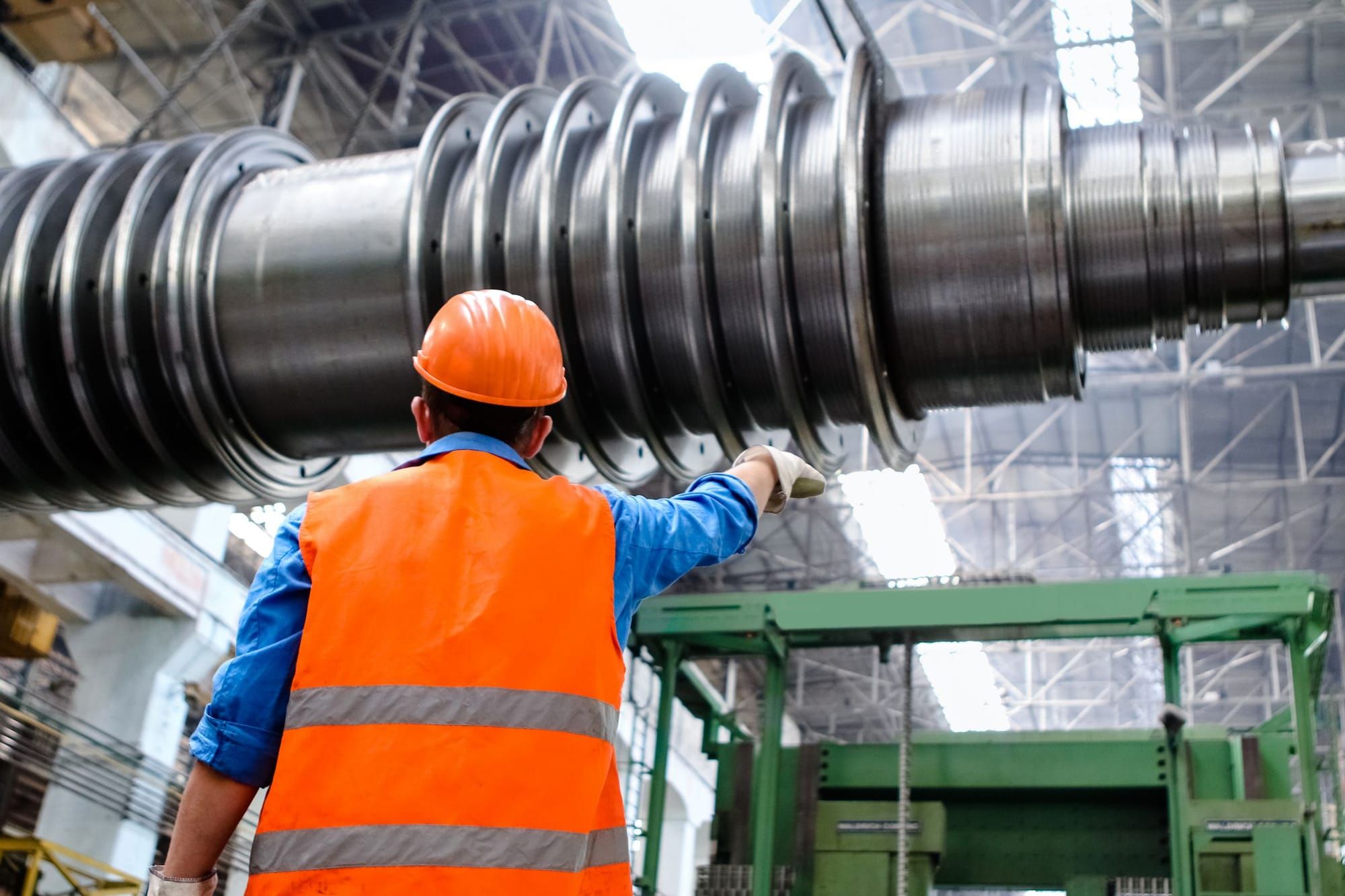 A worker in a hard hat and high-visibility vest beside a large machine shaft